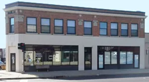 Two-story commercial building with large storefront windows on the ground floor and brick exterior on the upper level, located on a street corner.